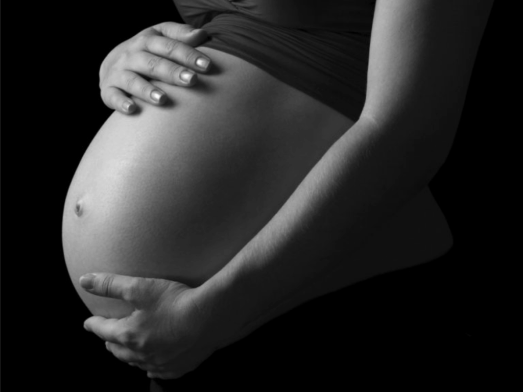 Black and white close-up of a pregnant belly with hands gently cradling it.