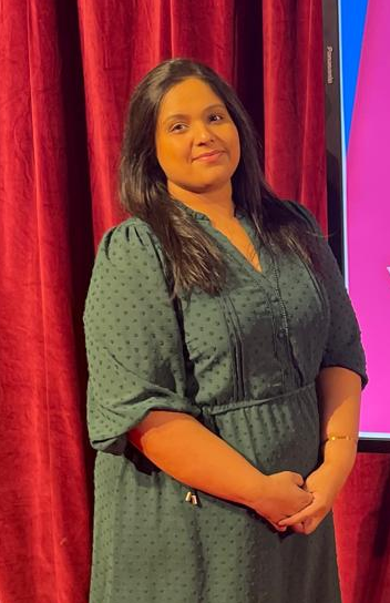 A woman in a green dress standing and smiling indoors.